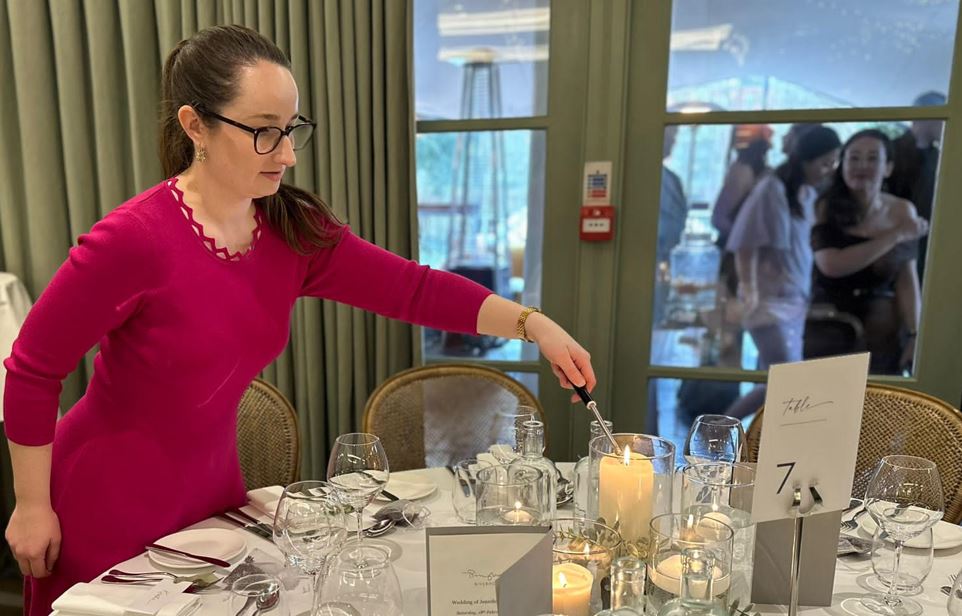 A wedding planner in a pink dress lighting candles on a wedding breakfast table