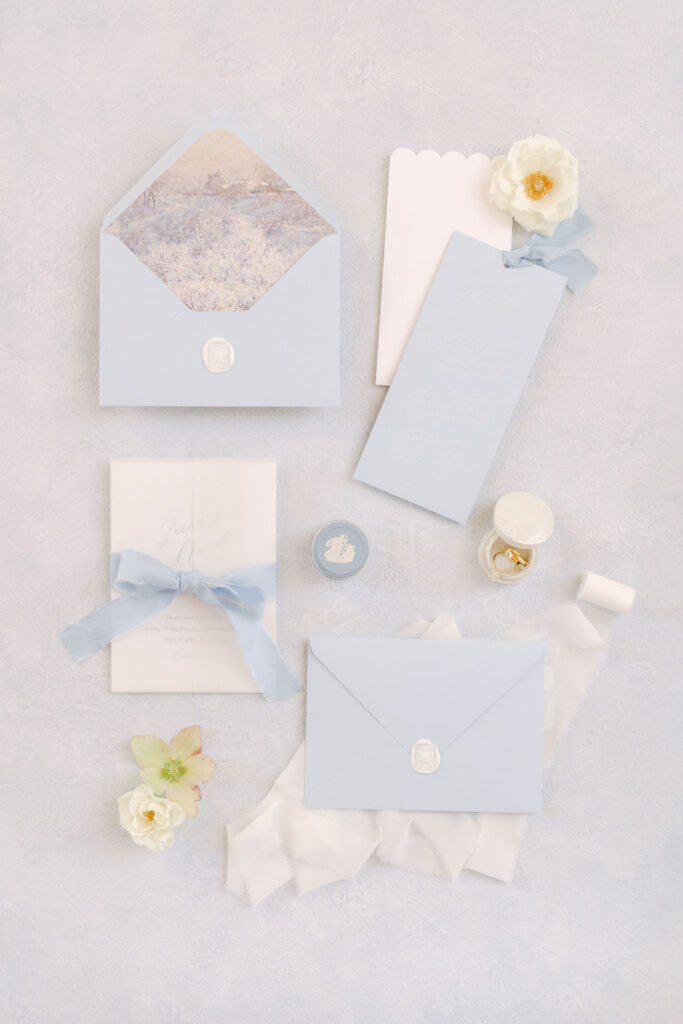 A fine art wedding flat lay photograph showing the blue and white wedding invitation suite on a blue background, featuring blue silk ribbons.