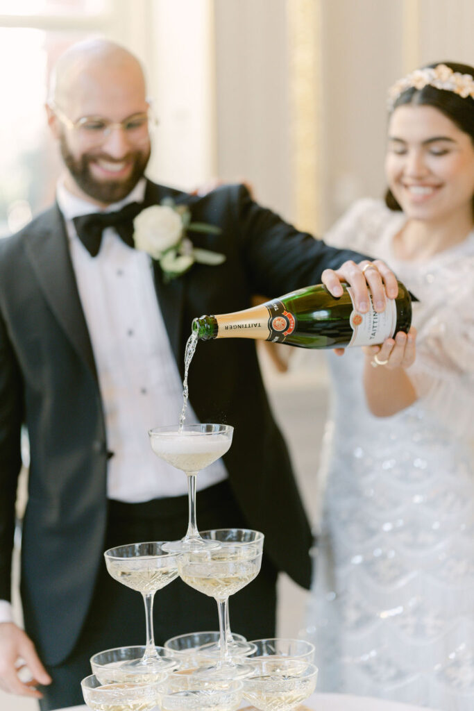 The bride and groom pour champagne into the top of a champagne tower in the reception room.