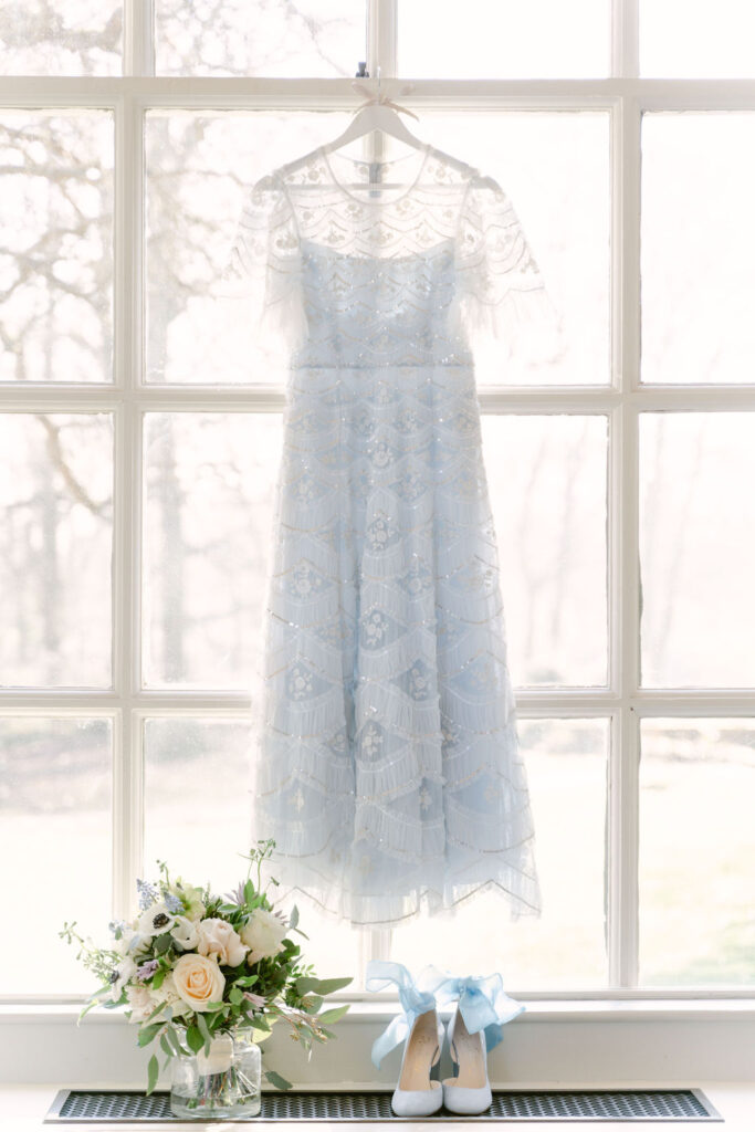 The bride's blue gown hanging in a window, with her shoes and bouquet displayed beneath.