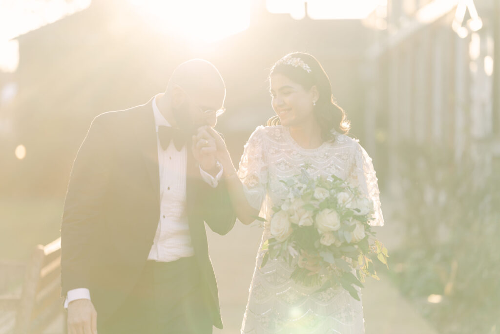 The groom kissing the bride's hand during golden hour.