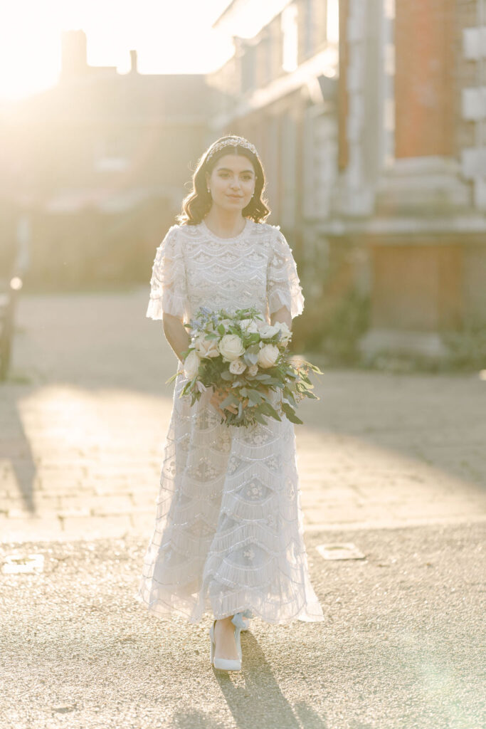 A bridal portrait featuring a full-length image of the bride in her ankle-length sparkly pale blue wedding gown, holding her bouquet during golden hour.