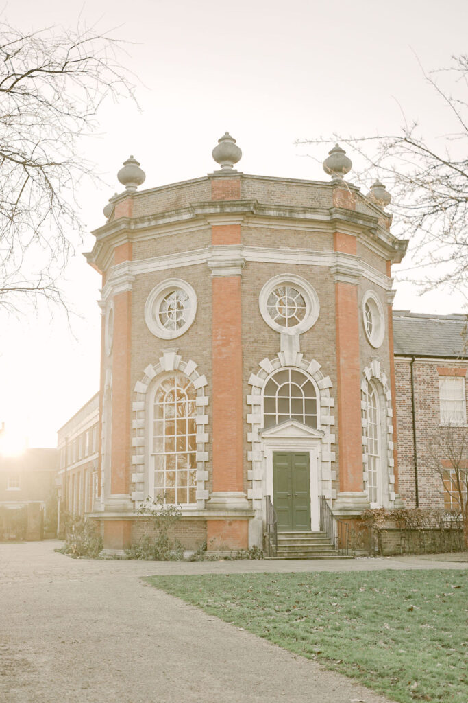 A portrait photograph of the exterior of the Octagon Room at Orleans House Gallery in Twickenham, London. A brick building with ornate windows and a green-painted wooden door which is perfect for a fine art style wedding.