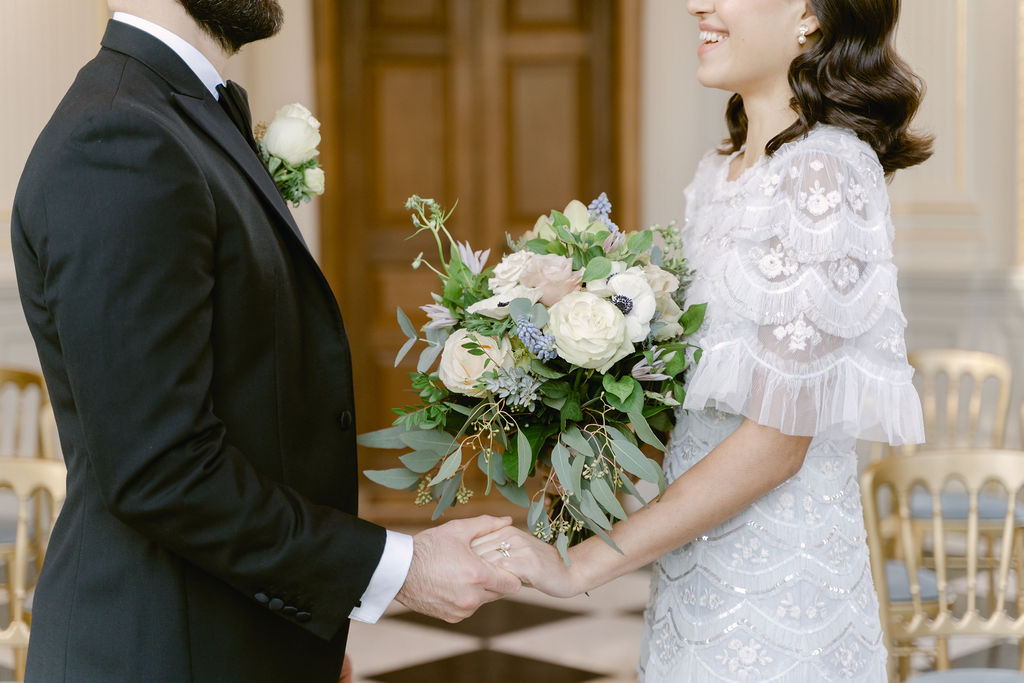 A landscape photograph of the bride and groom holding hands, featuring the brides bouquet of roses, hellebores, muscari, anemones and eucalyptus.