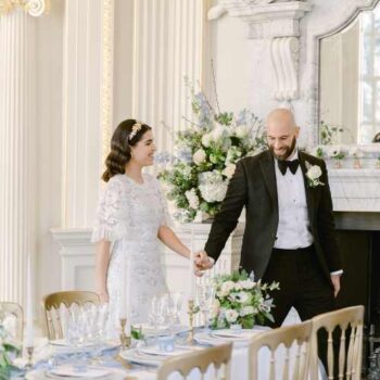 Bride and groom viewing their fine art style wedding reception table for the first time, in the Octagon Room at Orleans House Gallery. The room is Baroque in style and features a marble fireplace, black and white chequered floor and gold dining chairs.